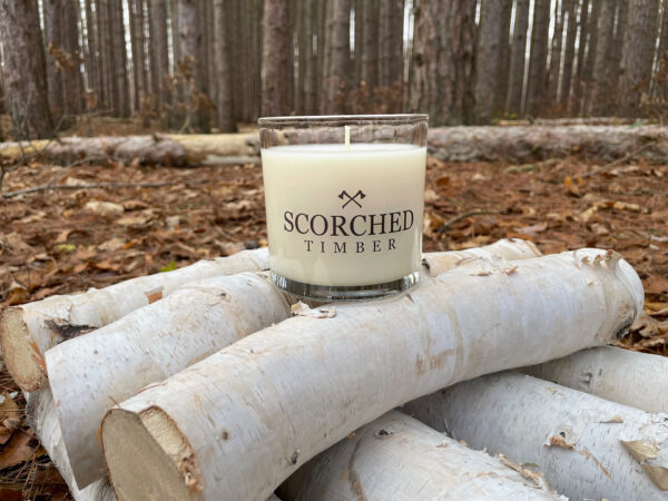 Large Scorched Timber Candle sitting on birch logs in a woods