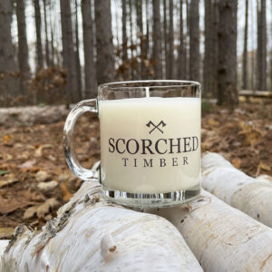 Scorched Timber Scented Candle Mug sitting on firewood in forrest